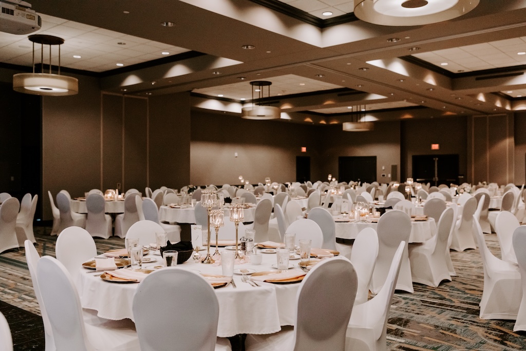 enormous large ballroom filled with tables and chairs covered in white cloth decorated for a wedding